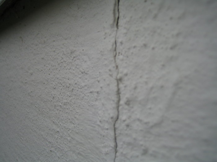 Spricka i vitmålad vägg utomhus, resultat av torrt väder, närbild.