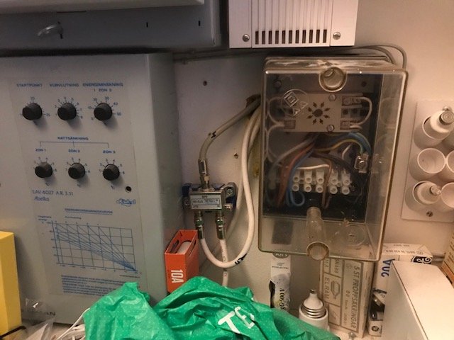 Elcentral med styrcentral, relä i plastlåda och diverse elektriska komponenter, mot en gipsvägg.