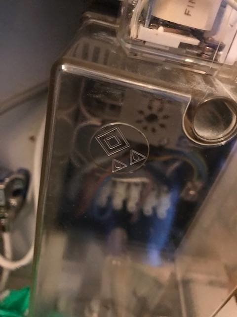 Närbild av en genomskinlig plastbox med ett relä och kablar, stansade symboler syns på framsidan.