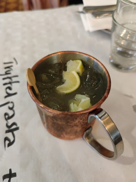 En moscow mule-cocktail i kopparmugg med limeskivor och is på ett bord.