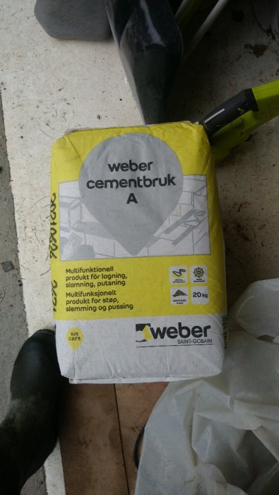 Säck med Weber cementbruk A på ett bygge med byggverktyg och gummistövel i bakgrunden.