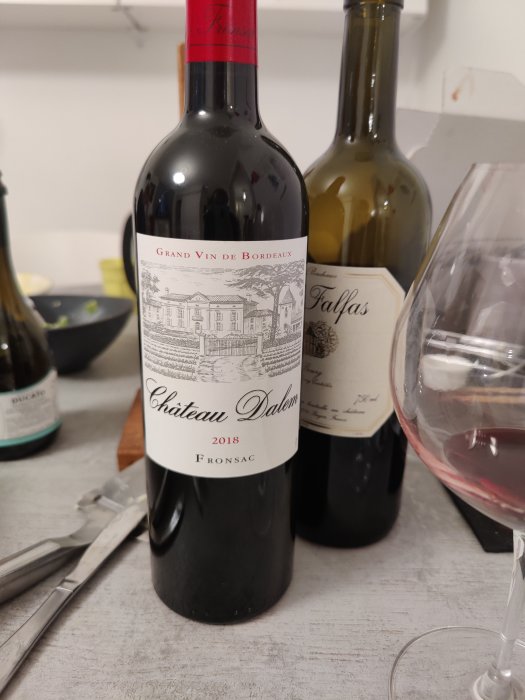 Flaska rödvin "Chateau Dalem 2018 Fronsac" framför en tom vinglas och en annan flaska.