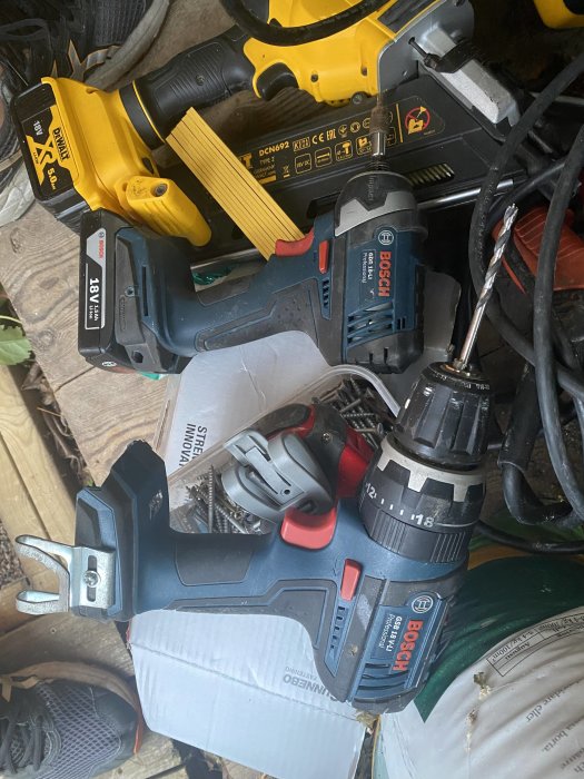 En samling verktyg inklusive en Bosch borr och en DeWalt slagskruvdragare på en arbetsyta.