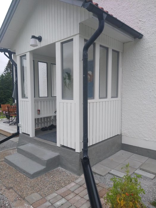 Nyligen installerade vita fönster på en farstubro med vit panel på ett hus.