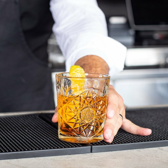 En cocktail i kristallglas serveras av en bartender, garnerad med en citronzest.