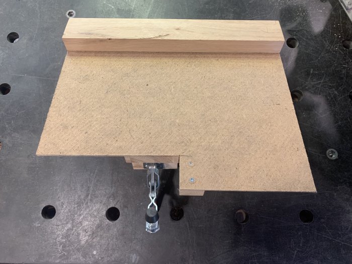 Custom-made cutting jig made of masonite and wood with a clamp on a workbench.