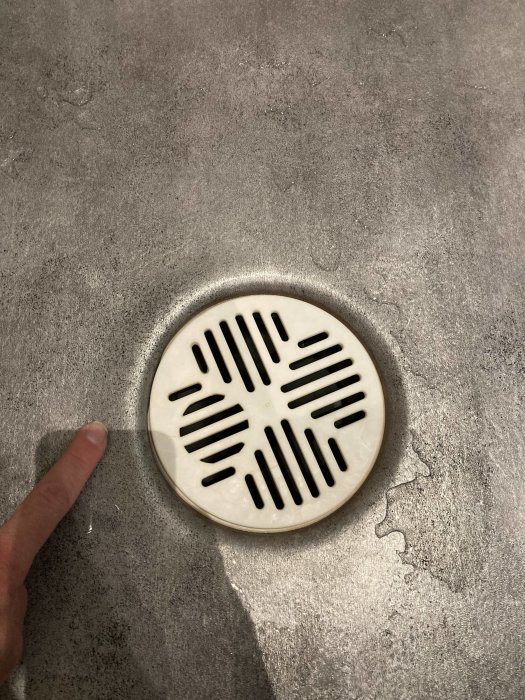 Plastmatta som släppt från klämringen runt en golvbrunn med synlig fingertopp.
