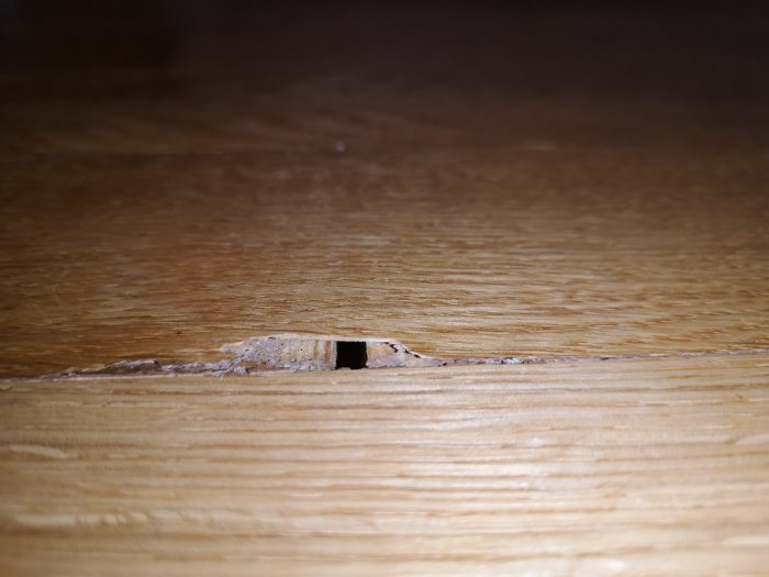 Skadad parkett med en tydlig springa och tecken på lossning, vilket visar golvproblem i bostadsrätt.