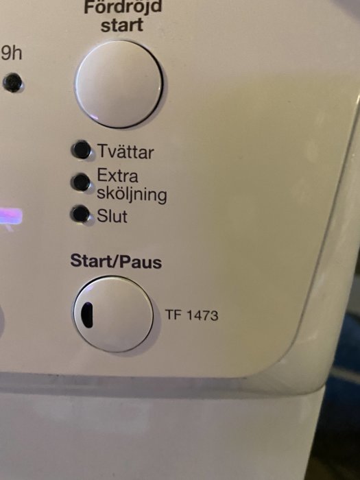 Närbild på en vit tvättmaskins kontrollpanel med startknappen och modellnummer TF 1473.