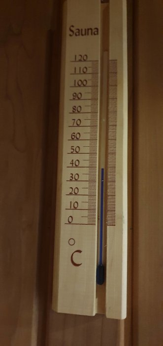 Bastutermometer i trä visar en temperatur kring 40 grader Celsius på en skala upp till 120 grader.