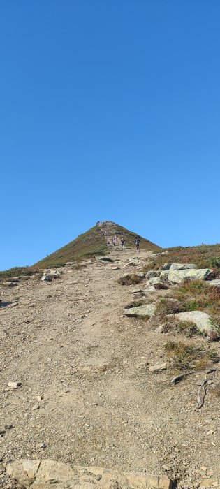 Vandrare på en stig upp mot toppen av ett berg med klarblå himmel.