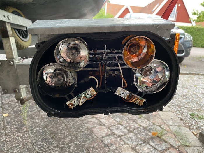 En öppen båttrailerlampa med rostiga LED-diodelar och synlig skada mot bakgrund av en uppfart.