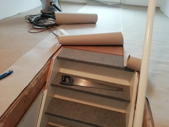 Oupplagt laminatgolv nära trappstart med synlig underlagsfoam och verktyg.
