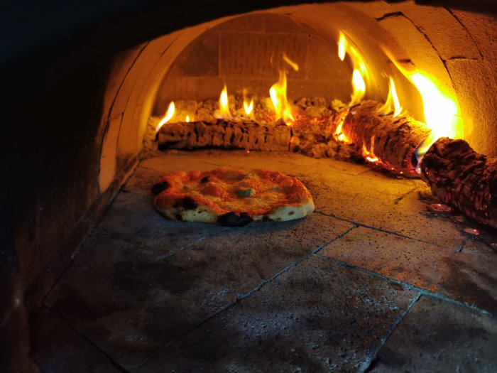 Pizza i en vedeldad ugn med levande flammor och glödande ved.