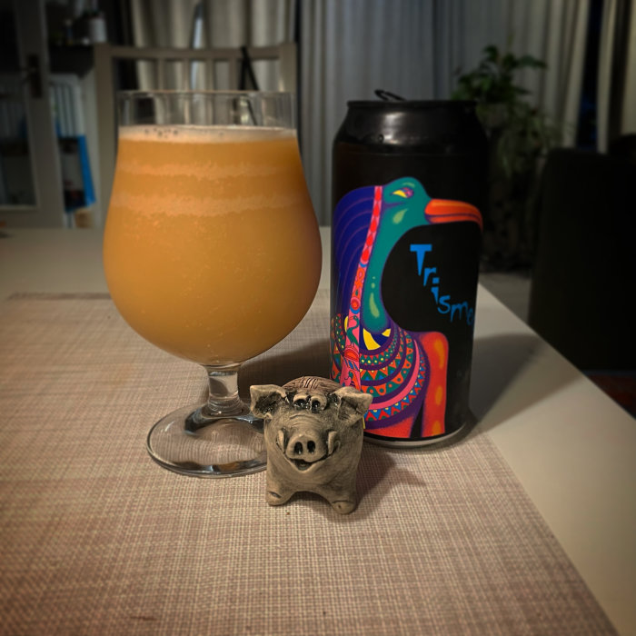 Ölglas fyllt med skummande dryck, färggrann ölburk och en liten prydnadsgris på ett bord.
