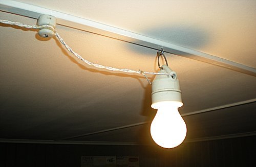 Glödlampa hänger från tak med synlig klamrad kabel längs en taklist.