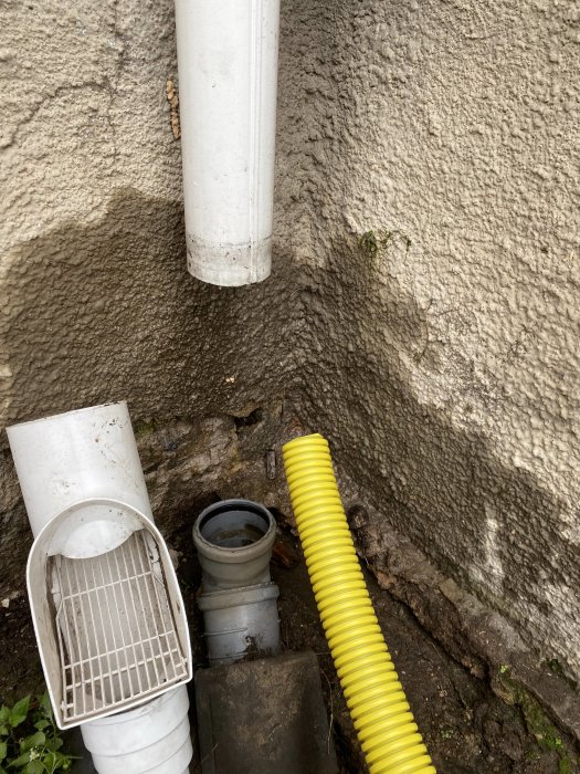 Avloppsrör och dräneringssystem vid husgrund med vattenfläckar på betongvägg.