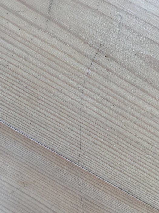 Närbild på vitvaxat furugolv med synliga repor och slitage.