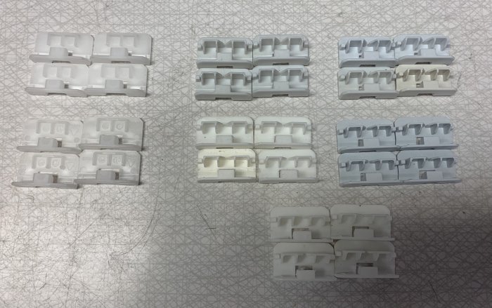 28 elektriska kabelklämmor i två olika utföranden på ett mönstrat underlag.