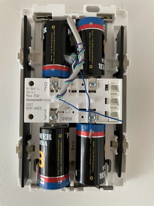 Öppnat dörrklocksystem på vägg visar ny och gammal ringklocka med anslutna kablar och batterier.