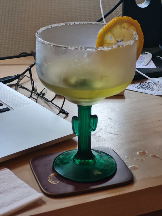 Margaritacocktail med saltkant och en skiva citron, på ett skrivbord.