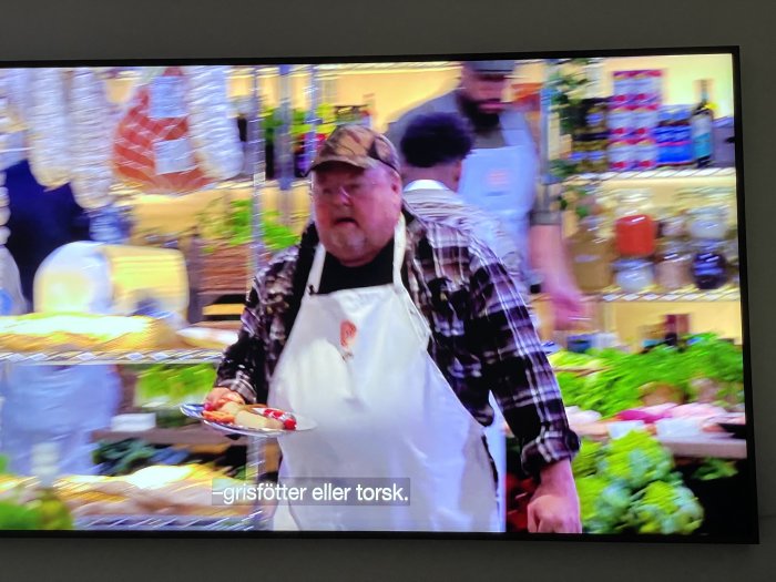 Man i förkläde bär matfat i en suddig och rörlig restaurangmiljö med textremsa nedtill.