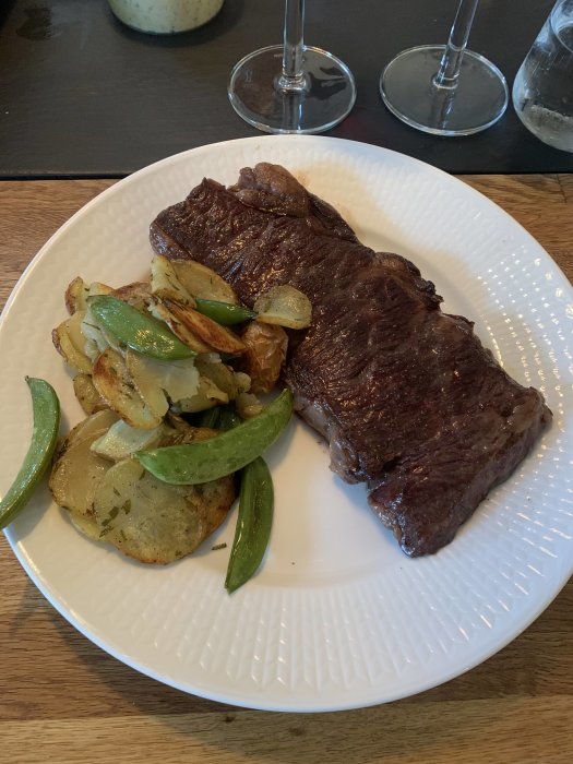 Grillad Zabutonbiff med stekt potatis och sockerärtor på en vit tallrik.