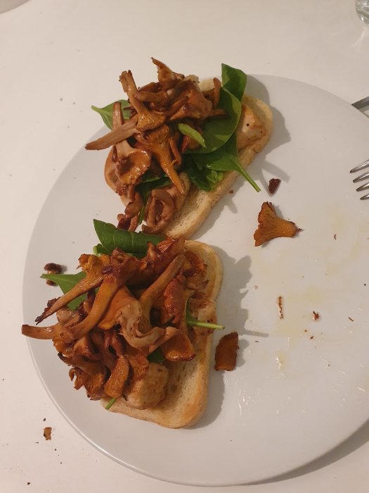 Rostat bröd med kyckling, babyspenat och smörstekta kantareller på en vit tallrik.