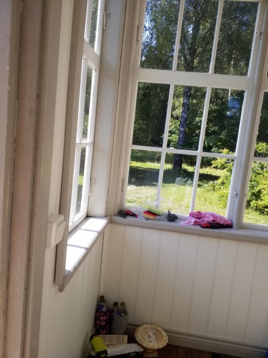 Oisolerad farstu med stora vita fönster och saker på fönsterbrädan, utsikt till trädgård, diskussion om tilläggsisolering.