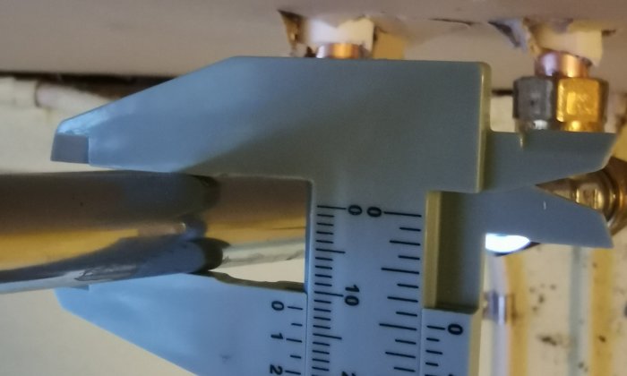 Skjutmått mäter tjocklek på rör, indikerar 10-12 mm, oskärpa i bakgrunden.
