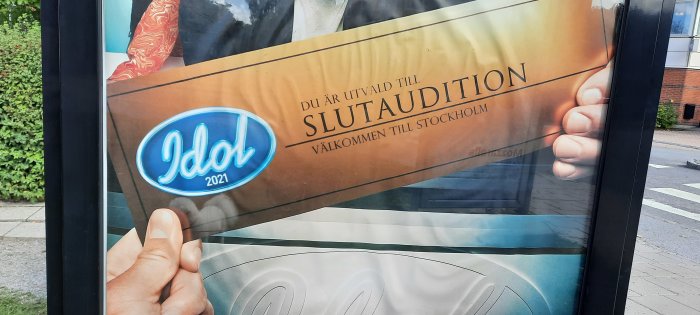 En hand som håller i en reklamskylt för "Idol 2021" med texten "du är utvald till slutaudition".