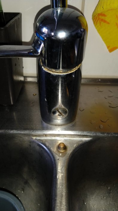 Kromad köksblandare med synlig anslutningsskruv ovanför en rostfri diskho.