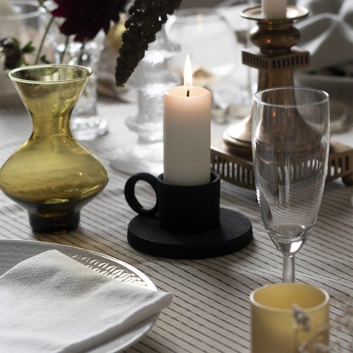 Ett traditionellt värmeljus i ljushållare på dukat bord med glas och dekorationer, nära ett värmeljus utan ljuslåga.