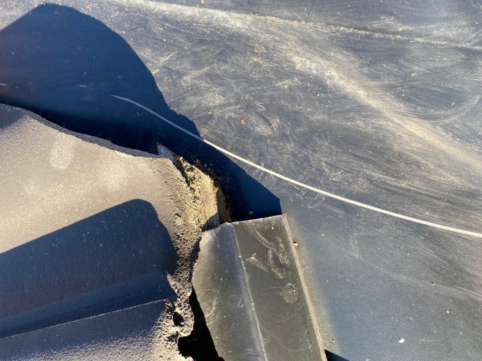 Åldrad, skadad läkt synlig vid foten av en takkupa där plåt och takpannor möts.