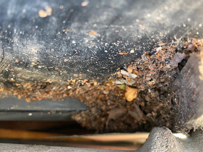 Något skadad takläkt med synlig röta och samlade löv och skräp vid en ränndals undersida.