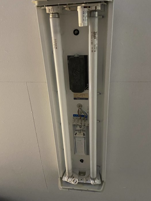 Öppnad lysrörsarmatur med två rör, tändare och elektrisk utrustning synlig.