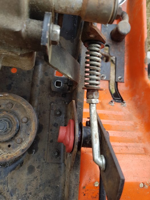 Modifierad kopplingsmekanism på en orange traktor, med en röd detalj till vänster och rostiga metalldelar.