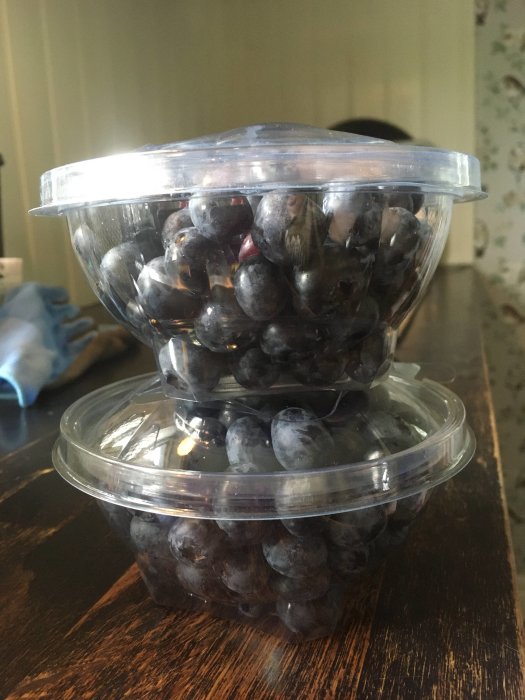 Två genomskinliga bunkar staplade med färska plommon på ett mörkt bord.