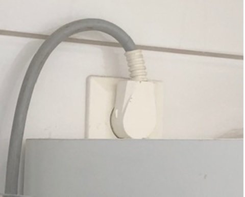 En vit varvtalsregulator med ansluten grå kabel på en vägg.