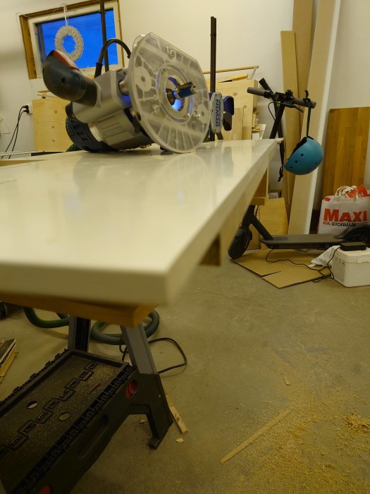 Handöverfräs vid kanten på en toppskiva i en verkstad med träspån och verktyg i bakgrunden.