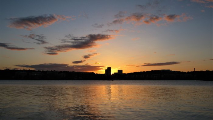 Solnedgång över en stadssiluett med spegling i vattnet.