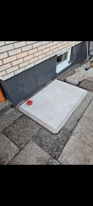 Betongplatta med avrundade hörn vid husgavel intill stuprör, förberedd för värmepumpinstallation.