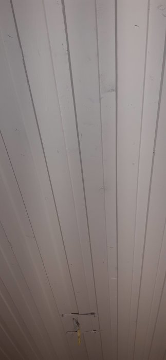 Vitmålad träpanel i tak med elektriska ledningar stående ut och tecken på förarbete.