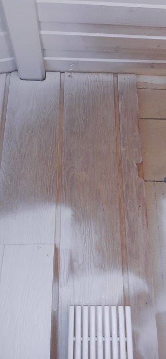 Trägolv under processen att målas vitt med spärrgrund applicerad, nära ett element och vägg.