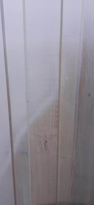 Vägg med träpanel halvvägs målad vit, sista lagret färg pågående, synliga glipor och knutar.