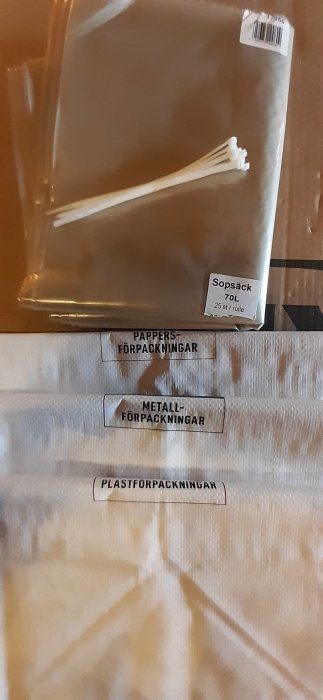 Sorteringspåsar för återvinning etiketterade för papper, metall och plast med sopsäckar och buntband.