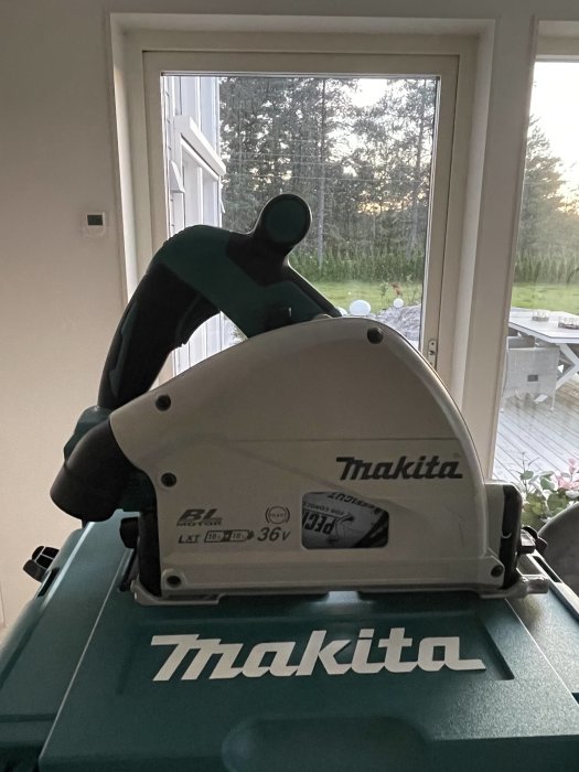 Makita cirkelsåg på Makita-väska framför fönster med utsikt över trädgården.