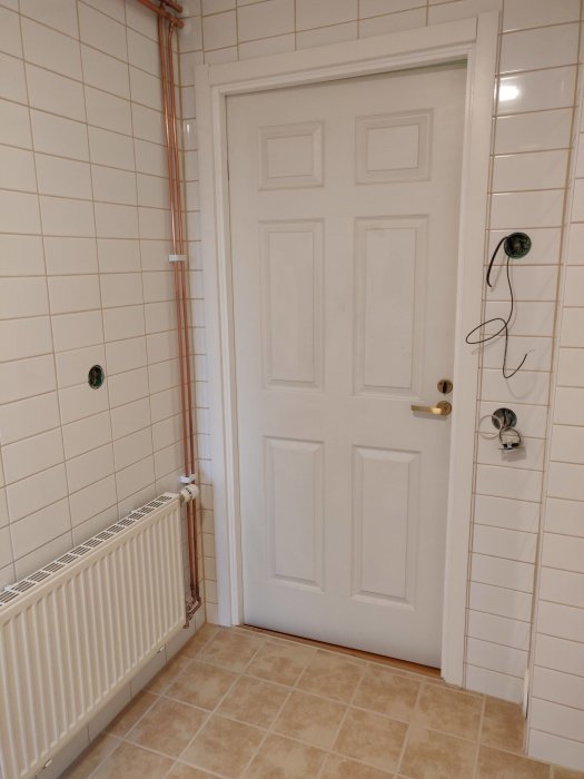 Nyrenoverat badrum med nyligen målad dörr, trimmad klacklist och täckbrickor på väggens rör.