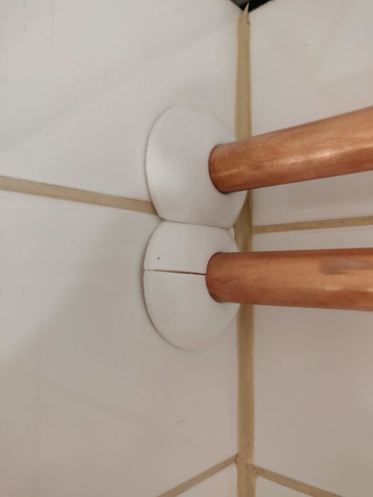 Två kopparfärgade rör med modifierade vita täckbrickor på en kaklad vägg.