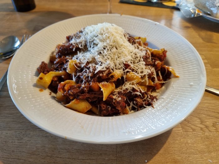 En tallrik med ragu och pasta toppat med riven parmesan.